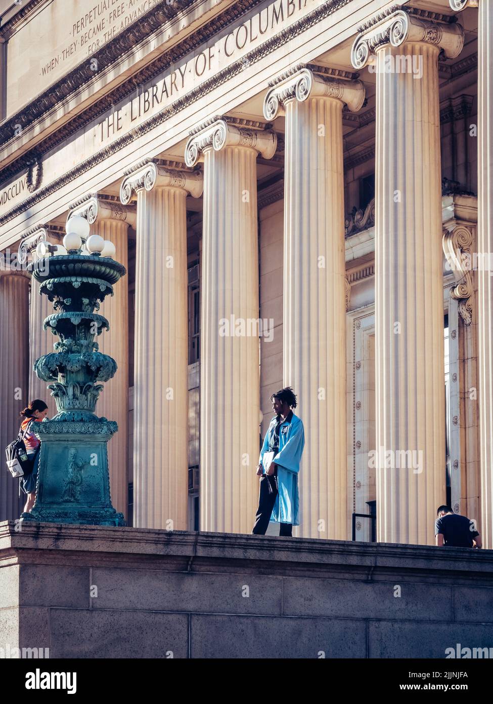 Eine vertikale Aufnahme einer Frau, die in einem Abschlusskleid an der Columbia University ein Foto von ihrer Freundin gemacht hat Stockfoto