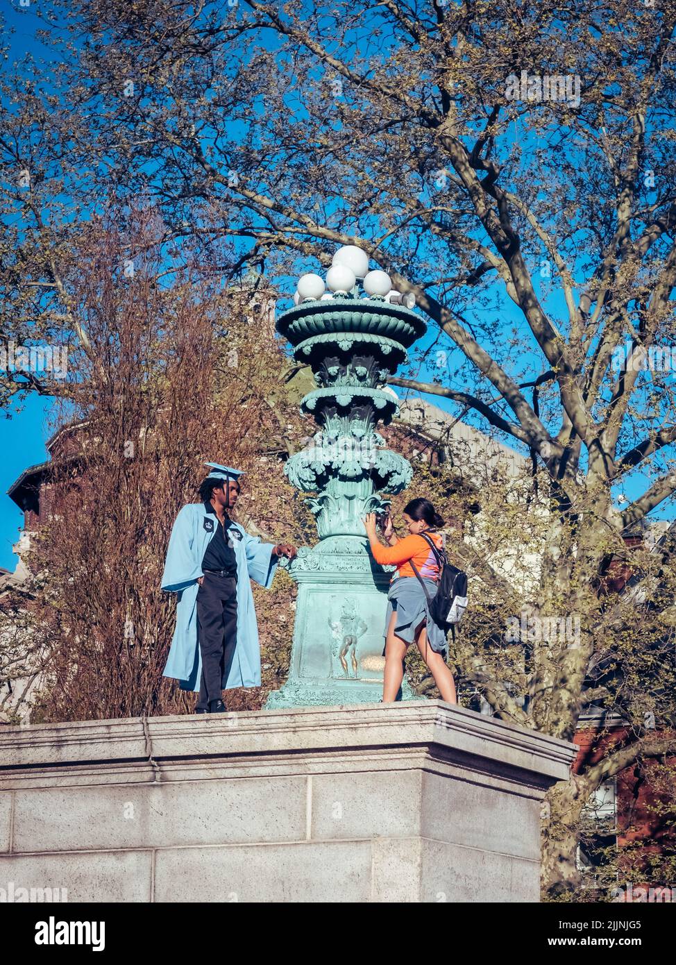 Eine vertikale Aufnahme einer Frau, die in einem Abschlusskleid an der Columbia University ein Foto von ihrer Freundin gemacht hat Stockfoto