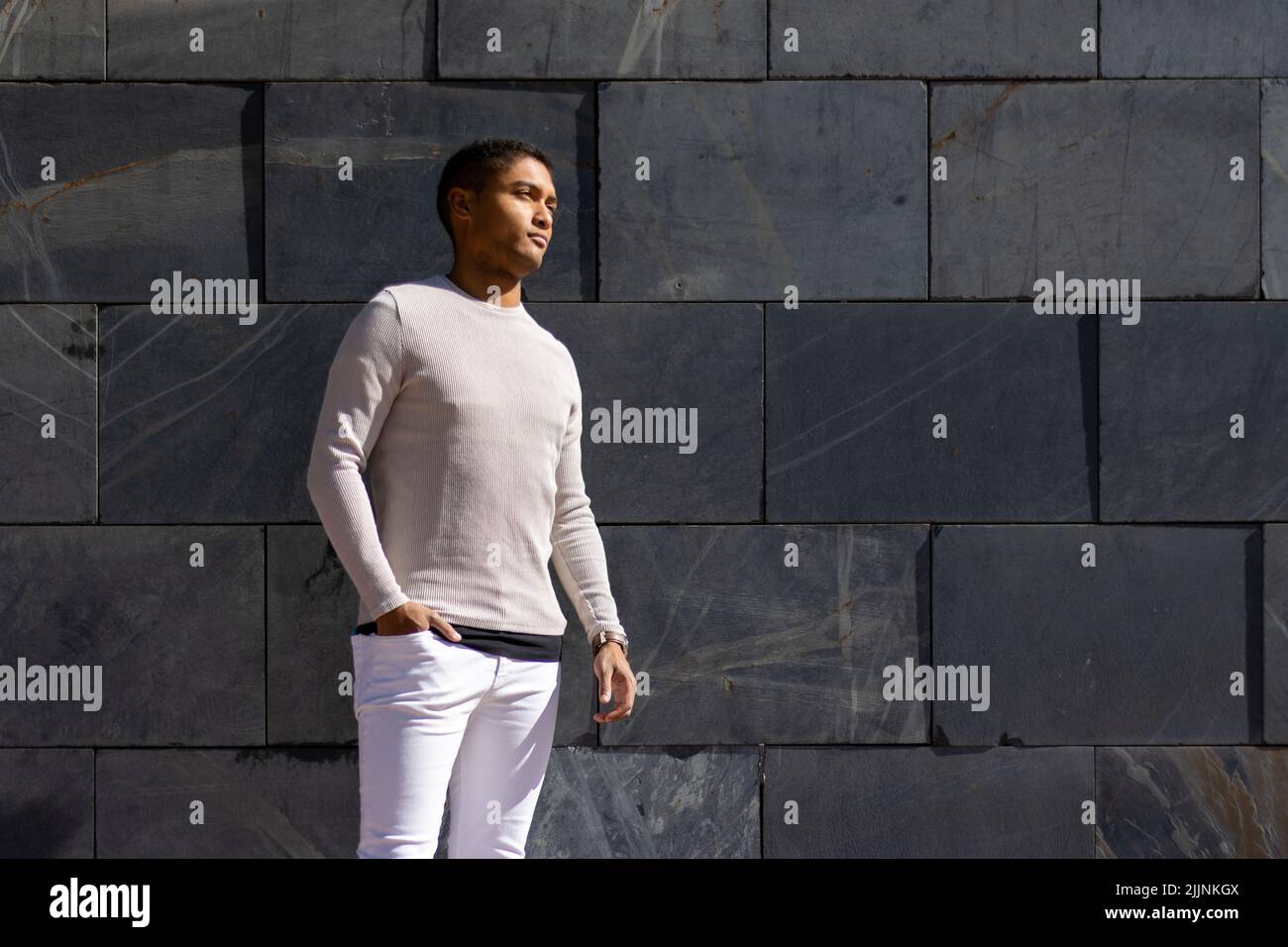Ein hispanischer Mann posiert in einer Hose und einem weißen Pullover auf horizontalem Plattenboden Stockfoto