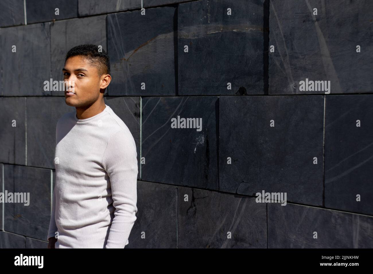 Ein hispanischer Mann posiert weißen Pullover, horizontalen Steinplatten Hintergrund mit Kopierer Platz Stockfoto