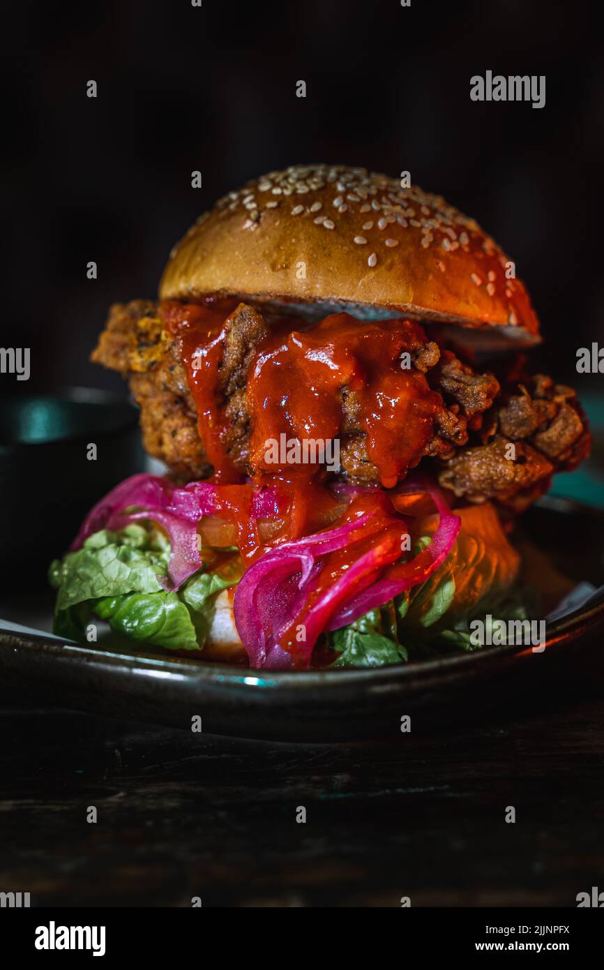 Eine vertikale Nahaufnahme eines Burgers auf einem dunklen Teller bei schwachem Licht Stockfoto