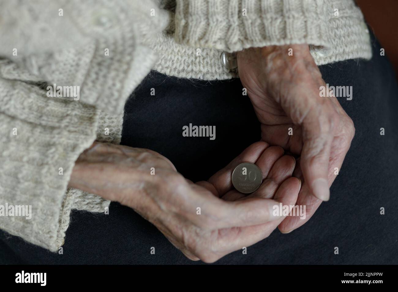 Die Hände einer Frau halten eine georgische Lari-Münze aus dem Jahr 50. Rente, Armut, soziale Probleme und das Thema Alter. Erhaltung. Stockfoto