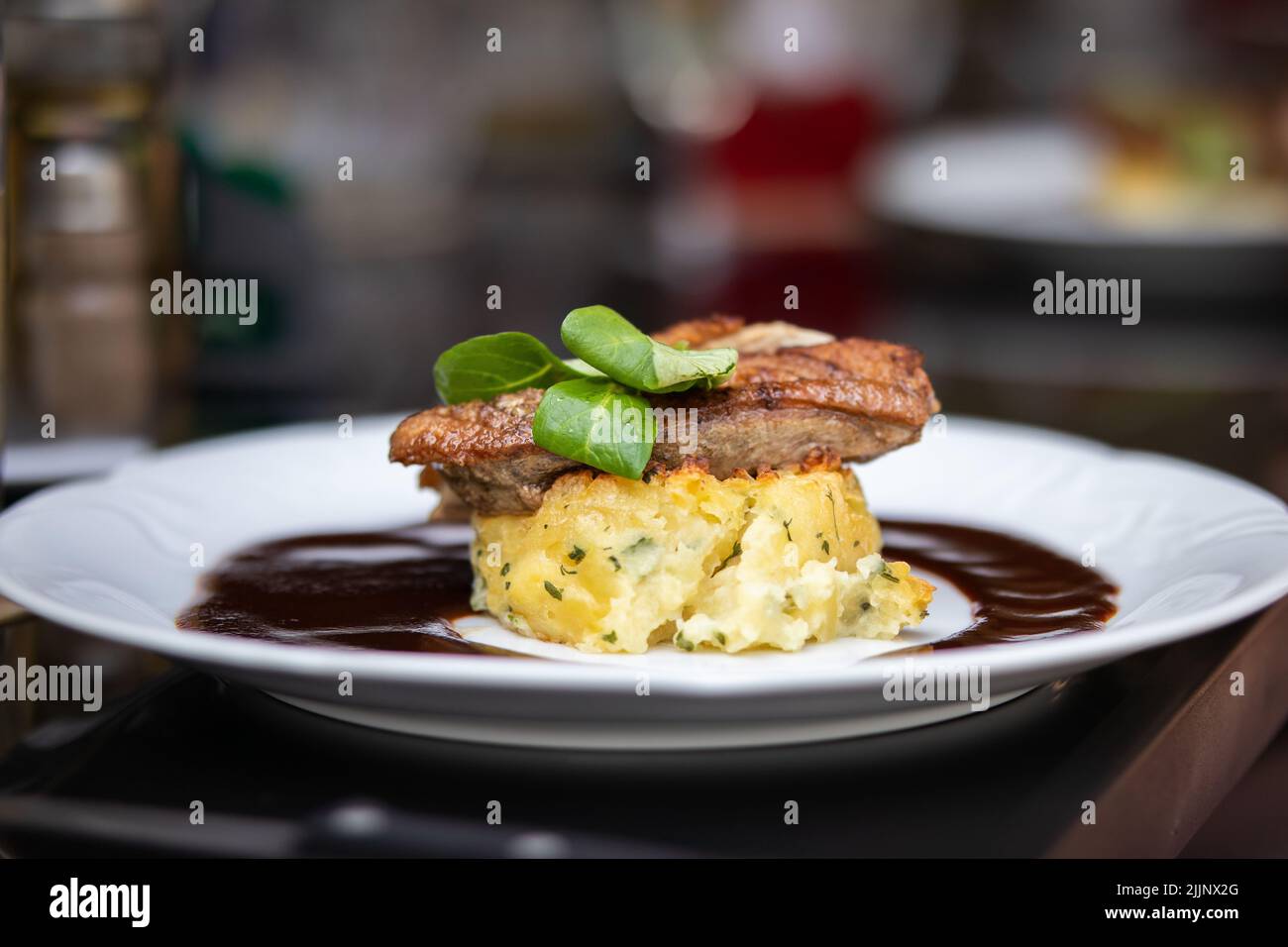 Appetitliches Essen auf einem weißen Teller in einem Restaurant. Geringe Schärfentiefe von gegrilltem Entenfleisch mit Gratinkartoffeln und Sauce. Stockfoto