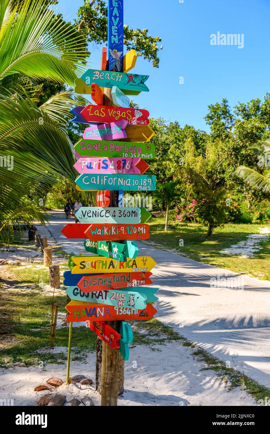 Farbenfroher Wegweiser an einer Fahrradstraße auf der tropischen Insel La Digue auf den seychellen. Schilder mit Hinweisen zu berühmten Reisezielen der Welt. Stockfoto