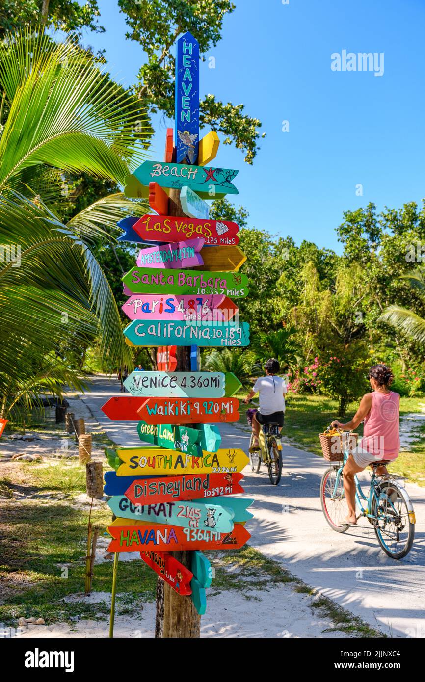 Bunte Schilder an einem Fahrradweg auf der tropischen Insel La Digue auf den seychellen. Schilder mit Hinweisen zu berühmten Reisezielen der Welt. Stockfoto