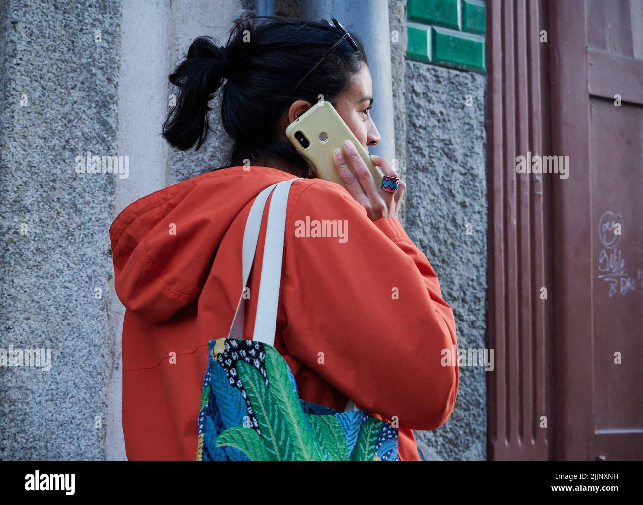 Ein junges spanisches Mädchen in einem orangefarbenen Hoodie, das draußen telefoniert Stockfoto