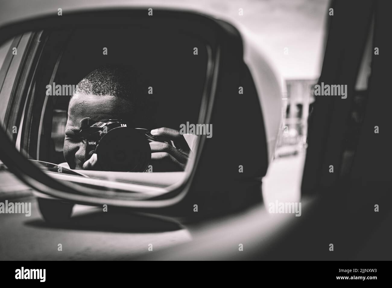 Eine Graustufenaufnahme des Selbstporträts eines Fotografen auf der Spiegelung des Seitenspiegels eines Autos Stockfoto