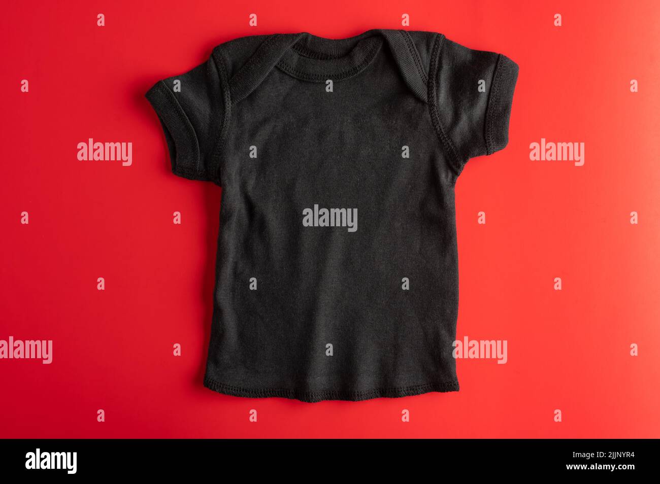 Flaches Modell eines schwarzen T-Shirts aus Baumwolle für Kinder auf rotem Hintergrund. Sport bequeme Kleidung für Mädchen. Layout zum Auftragen von Drucken, Logos. Wer Stockfoto