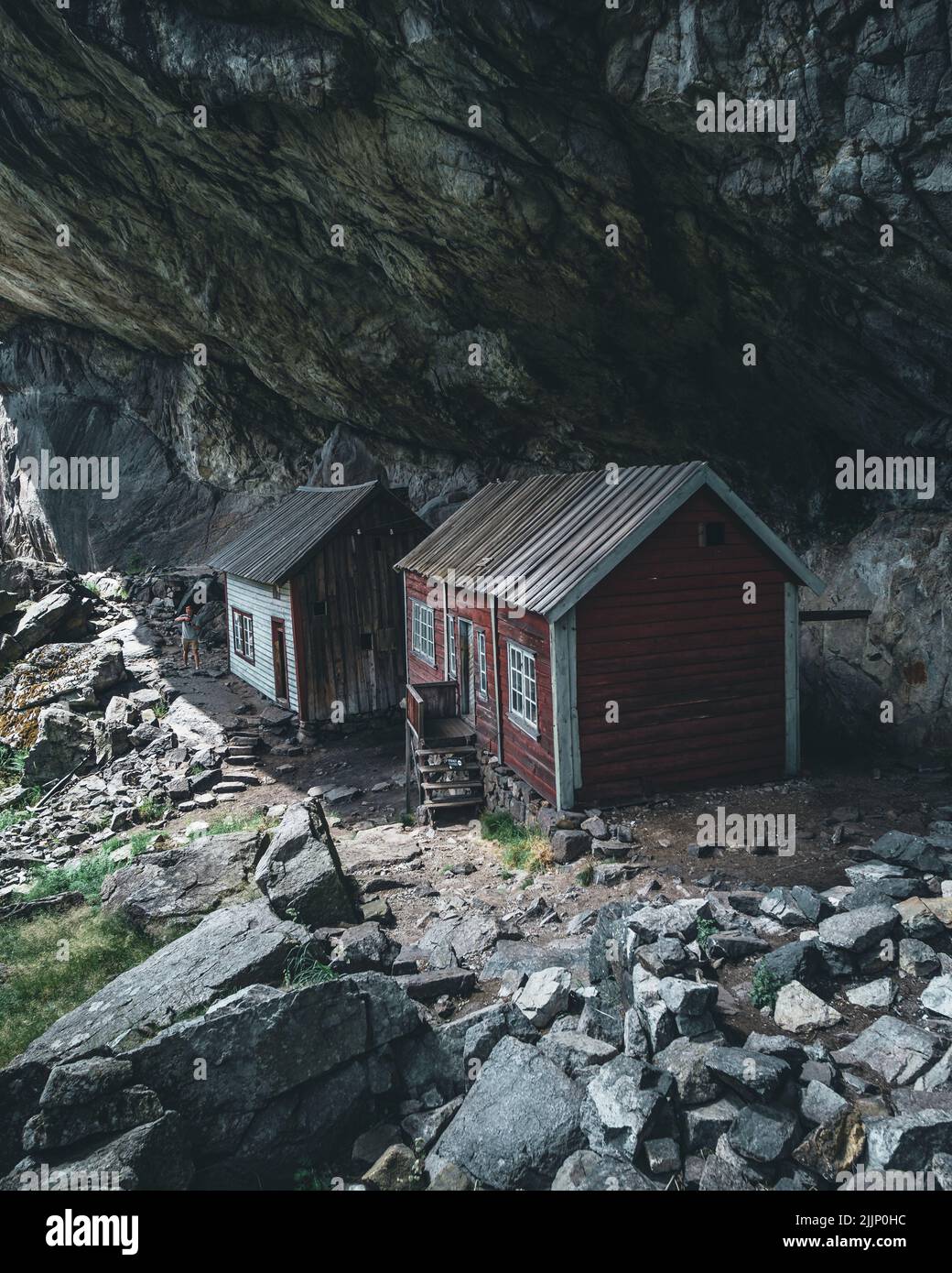 Vertikale Aufnahme von zwei kleinen Häusern unter dem großen Bergfelsen Stockfoto