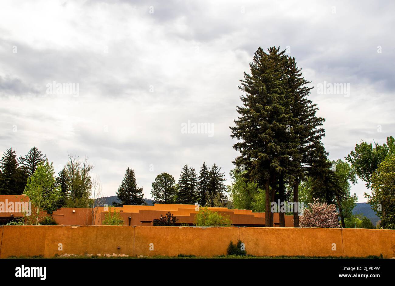 Orangefarbene Stuckwände und Gebäude in Taos New Mexico USA mit hohen Pinien und blauen Bergen in der Ferne Stockfoto