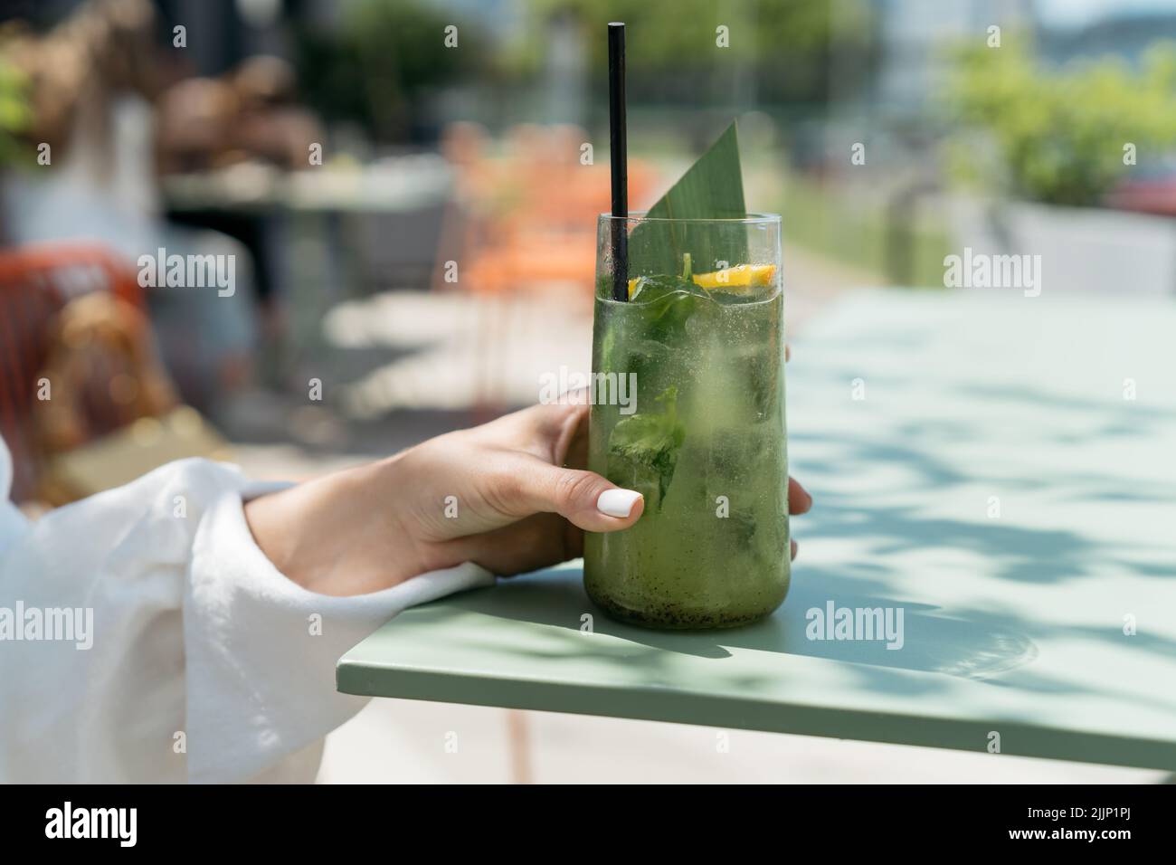 Frau, die in einem Café im Freien sitzt und einen Cocktail trinkt Stockfoto