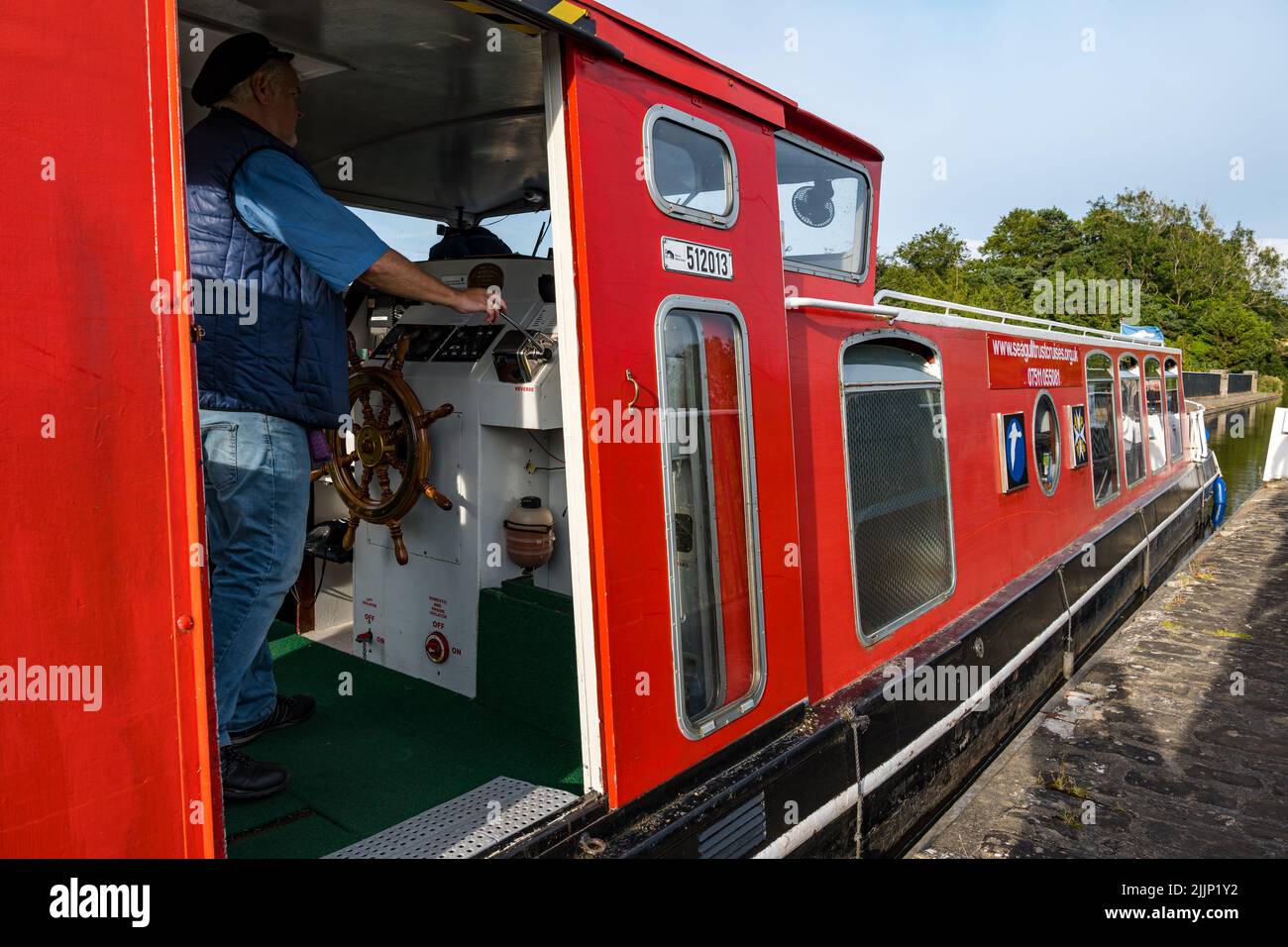 Schottland, Vereinigtes Königreich, 27.. Juli 2022. UK Wetter: Sonniger Abend auf dem Union Canal. Ein Schmalboot auf dem Kanal steuert einen Aquädukt, wobei der Kapitän des Hausbootes das Kapitänsrad steuert Stockfoto