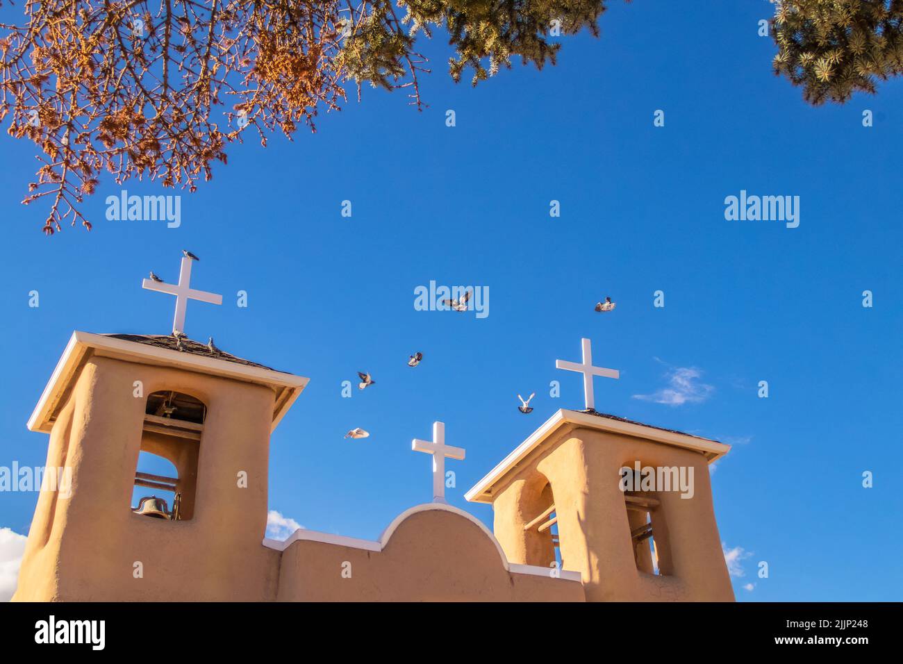Pidgeons fliegen über dem Dach und den Glockentürmen der berühmten adobe San Francisco de Asis Mission Church auf dem hauptplatz von Ranchos de Taos, New Mexi Stockfoto