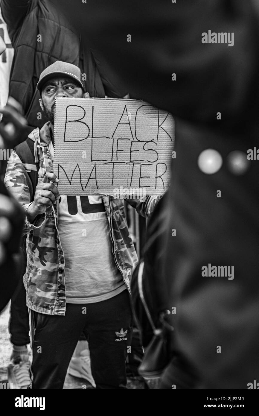 Eine vertikale Graustufenaufnahme eines Mannes, der während des Protestes in Glasgow, Großbritannien, ein Schild mit der Aufschrift „BLACK LIFES MATTER“ hält Stockfoto