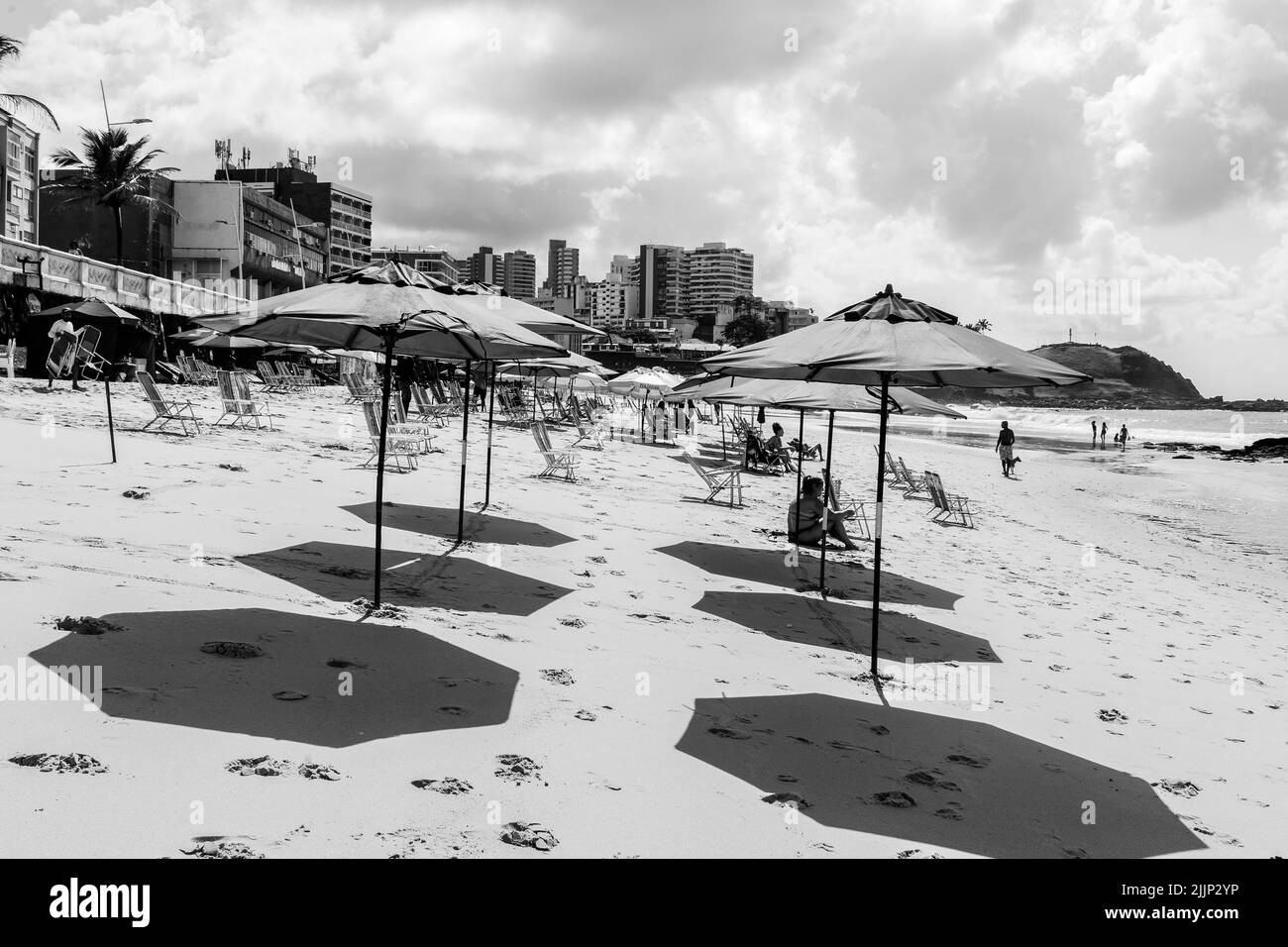 Ein grauer Sonnenschirm mit Schatten auf Sand am Strand Farol da Barra in Salvador, Bahia, Brasilien. Stockfoto