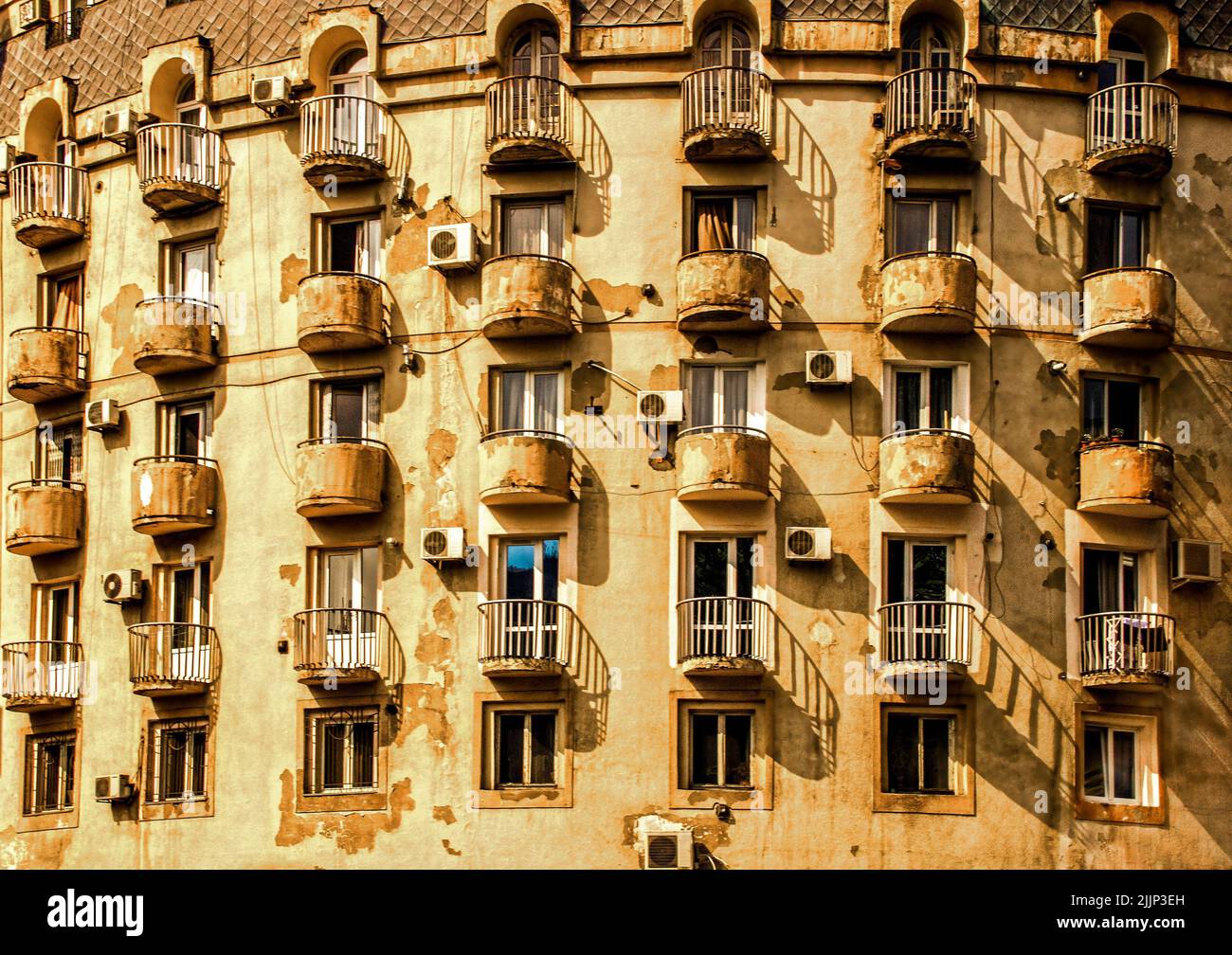 Abgerundete Balkone auf abgerundeten Gebäude in Tiflis Georgia Eurasia mit abblätterndem Gips und Klimaanlage, die ein strukturiertes Muster bilden. Stockfoto