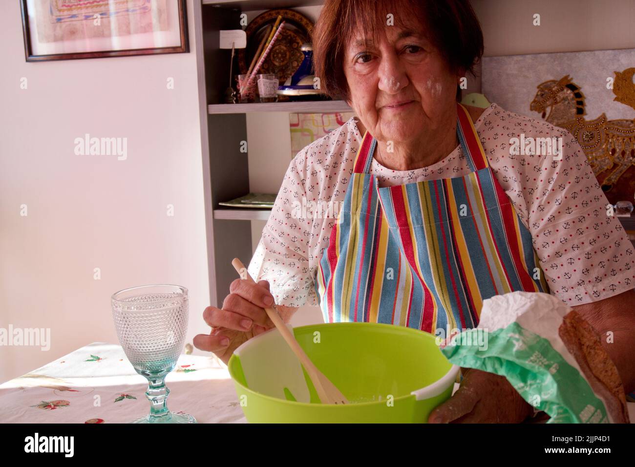 Eine ältere weiße Dame, die zu Hause Kuchen mit Mehl und Eiern backt Stockfoto
