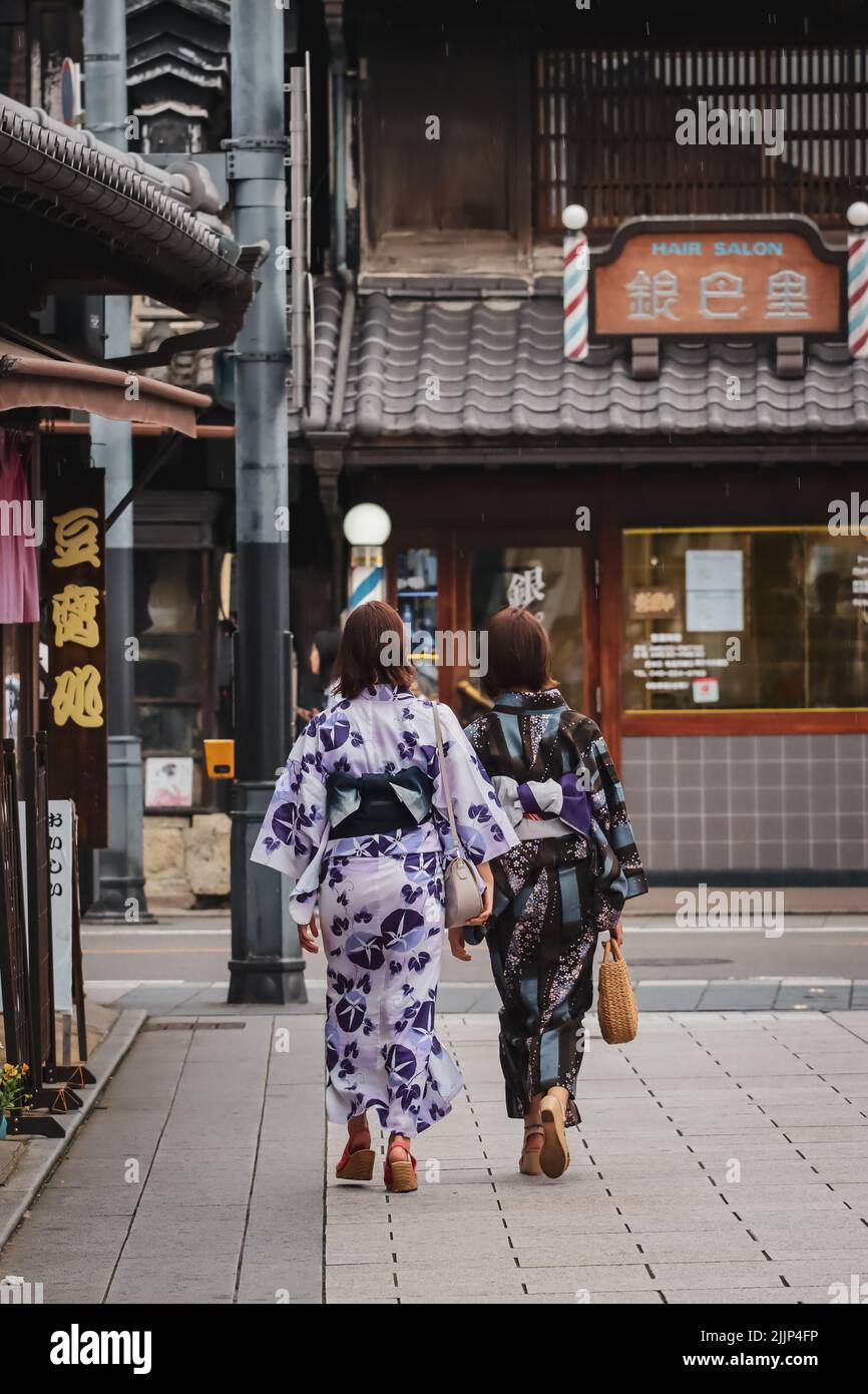 Eine vertikale Aufnahme von zwei modischen japanischen Frauen, die auf der Straße spazieren Stockfoto