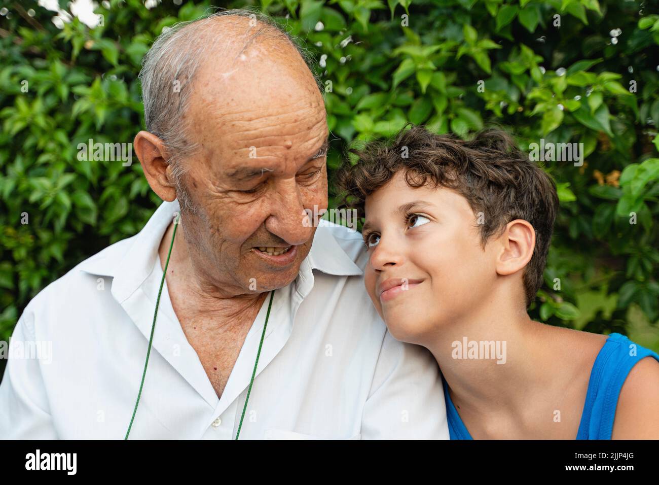 Großvater und EnkelGroßvater und Enkel tauschen liebevolle Blicke aus, die draußen sitzen - multigenerationales Familienmenschen-Lifestyle-Konzept Stockfoto