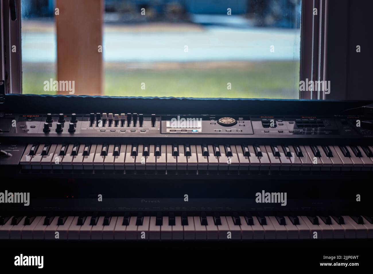 Eine Nahaufnahme von Klaviertasten mit zwei Zeilen auf Musikinstrumenten mit einem Fenster im Hintergrund Stockfoto