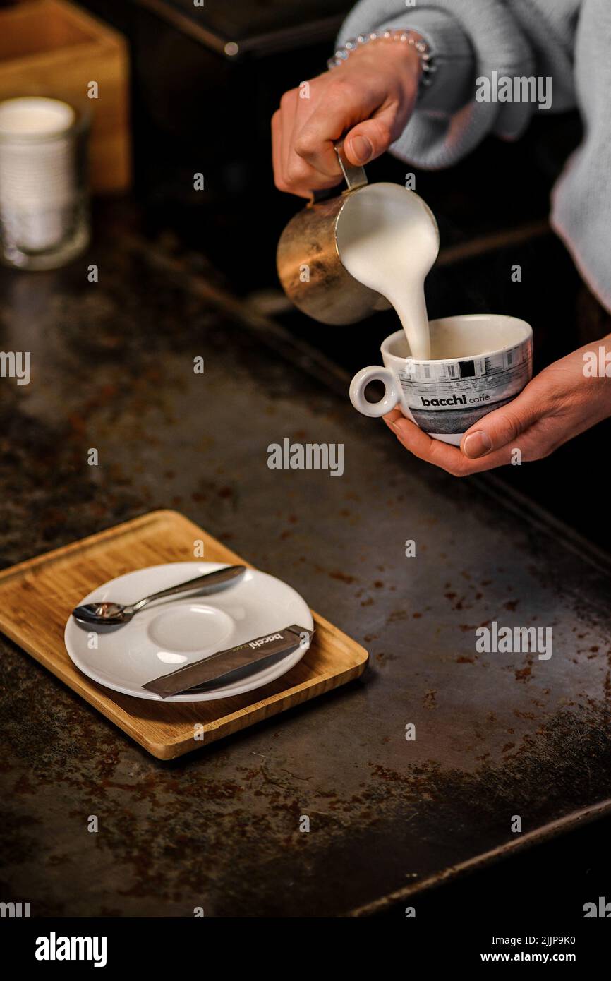 Eine vertikale Aufnahme einer Frau, die während ihrer Kaffeepause Milch in eine Tasse in einem Café gießt Stockfoto