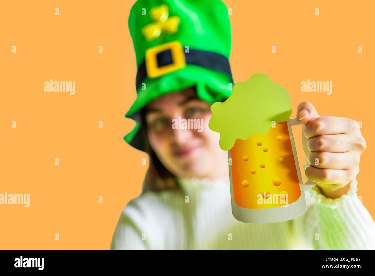 Eine Nahaufnahme des St. Patrick's Day Kobold Model Mädchens mit einem Becher Bier auf orangefarbenem Hintergrund Stockfoto