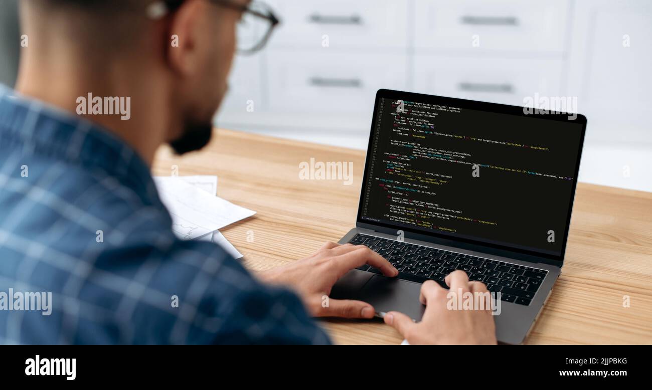 IT-Technologie. Panoramafoto eines Programmierers mit Laptop. Blick über die Schulter eines Mannes, eines IT-Spezialisten auf einen Laptop-Bildschirm, ein männlicher Programmierer schreibt Codes für eine Anwendung vor, entwickelt Software Stockfoto