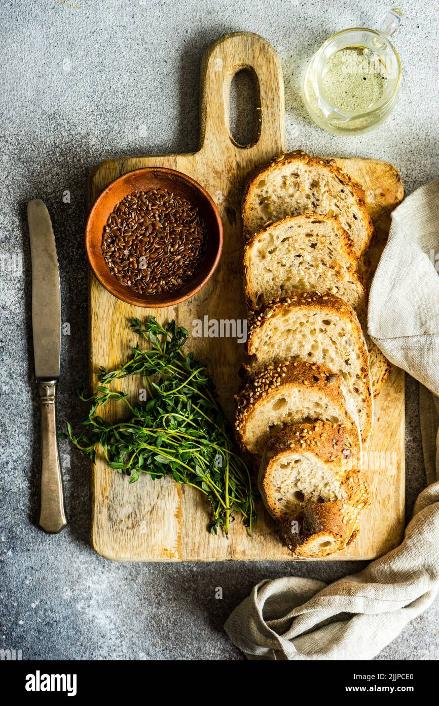 Draufsicht auf Scheiben braunes Brot mit Olivenöl, Leinsamen und Thymian auf einem Schneidebrett Stockfoto