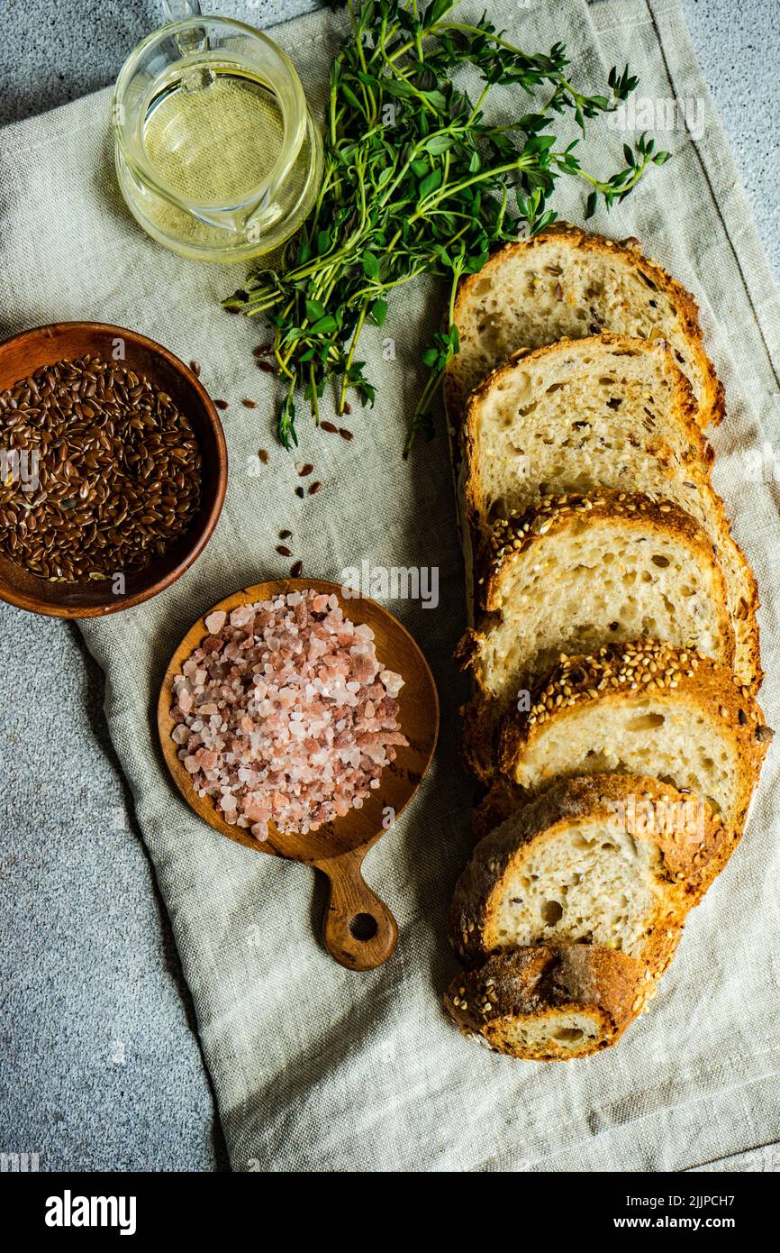 Draufsicht auf Scheiben von braunem Brot mit Olivenöl, Leinsamen, Thymian und rosa Himalaya-Salz auf einem gefalteten Geschirrtuch Stockfoto