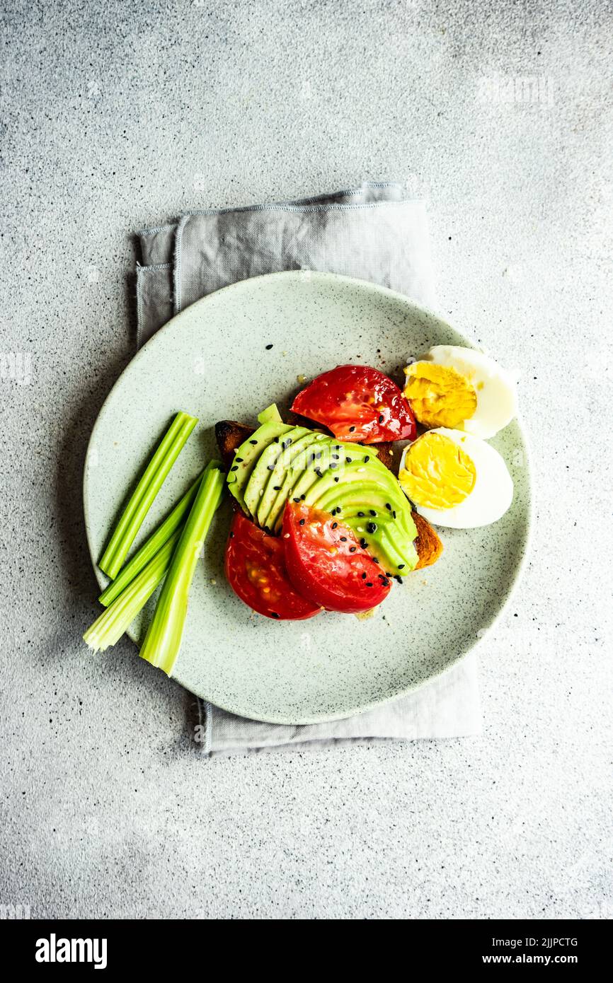 Ansicht von oben auf eine Scheibe Avocado-Toast mit Tomaten, gekochtem Ei, Sellerie-Sticks und Sesamsamen Stockfoto