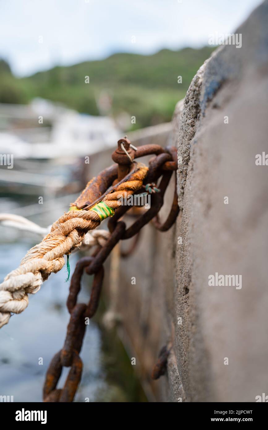 Eine vertikale Aufnahme einer braunen Schnur mit einem rostigen Metall, das auf einem Stein auf einem unscharfen Hintergrund hängt Stockfoto