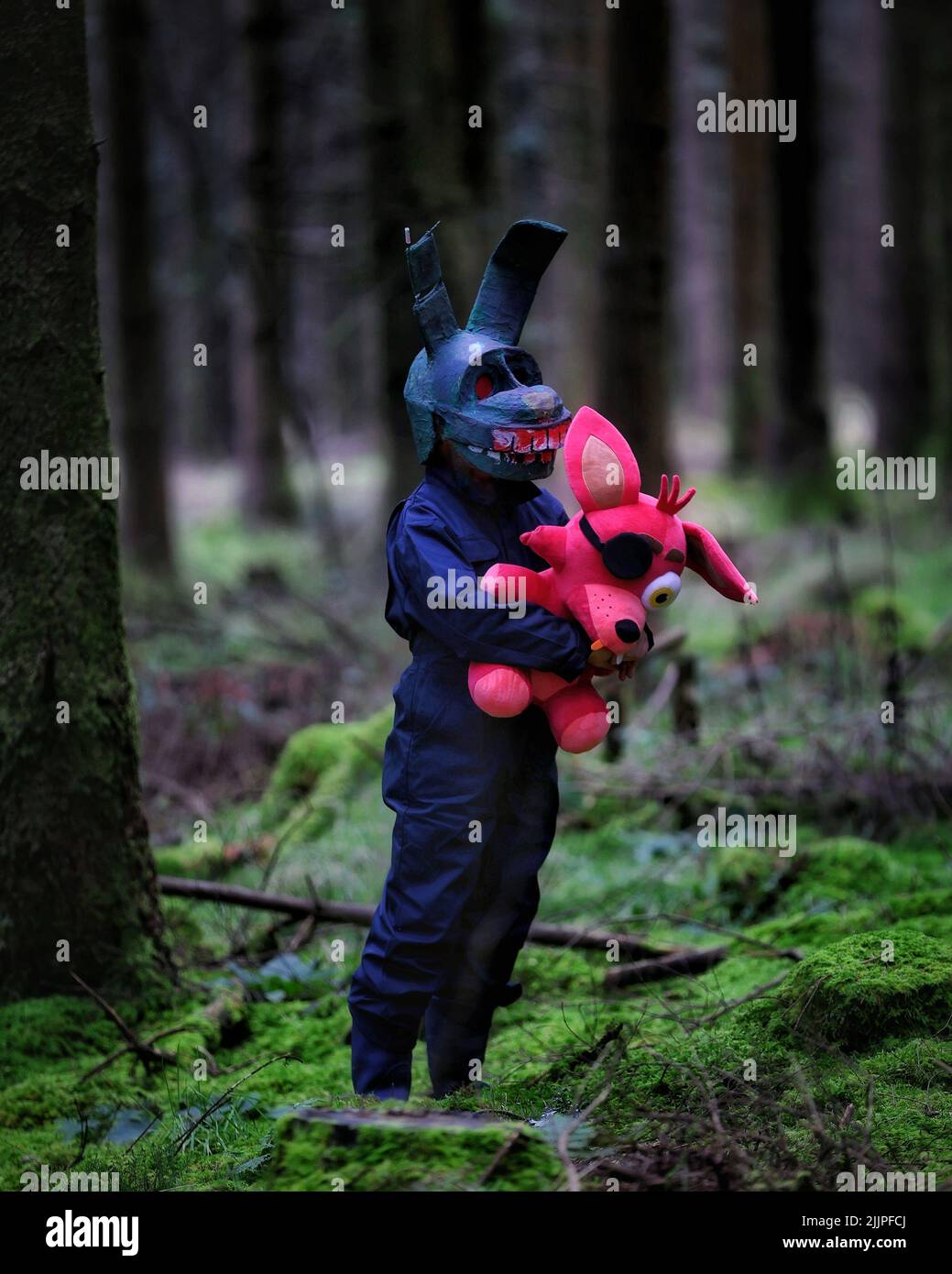 Eine vertikale Aufnahme eines Mannes, der ein gruseliges Kaninchenkostüm trägt und mitten im Wald ein Piratenkaninchen in der Hand hält Stockfoto