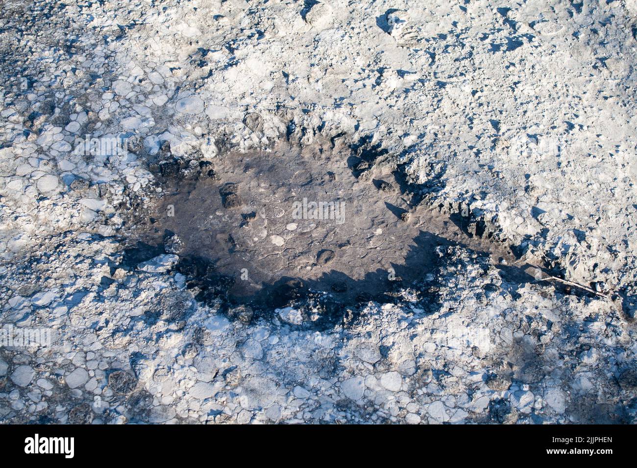 Eine Nahaufnahme von schneebedecktem Boden mit flüssigem Kreis in der Mitte mit Sonnenlicht Stockfoto