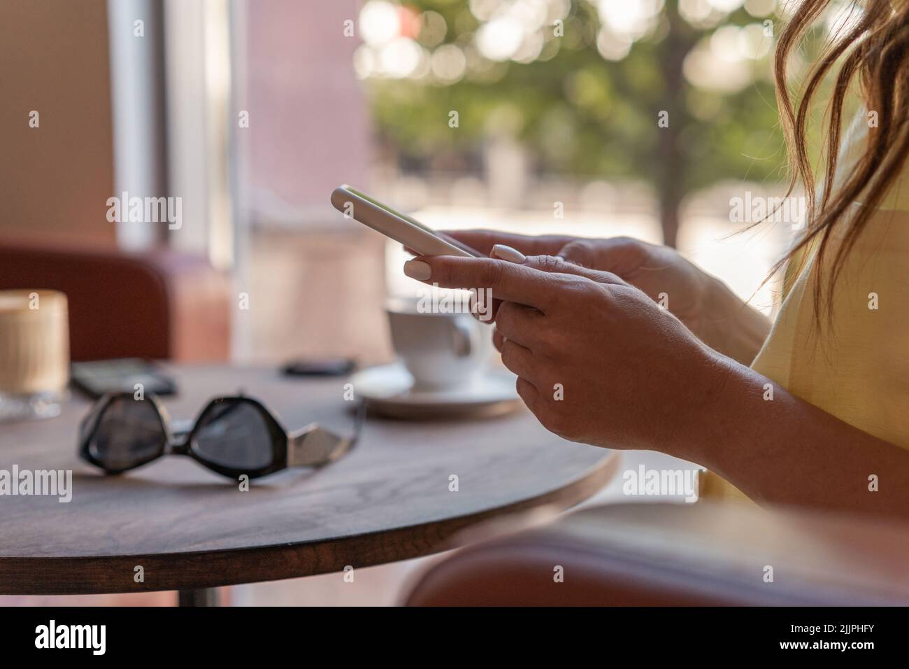 Nahaufnahme einer Frau, die mit einem Mobiltelefon in einem Café sitzt Stockfoto