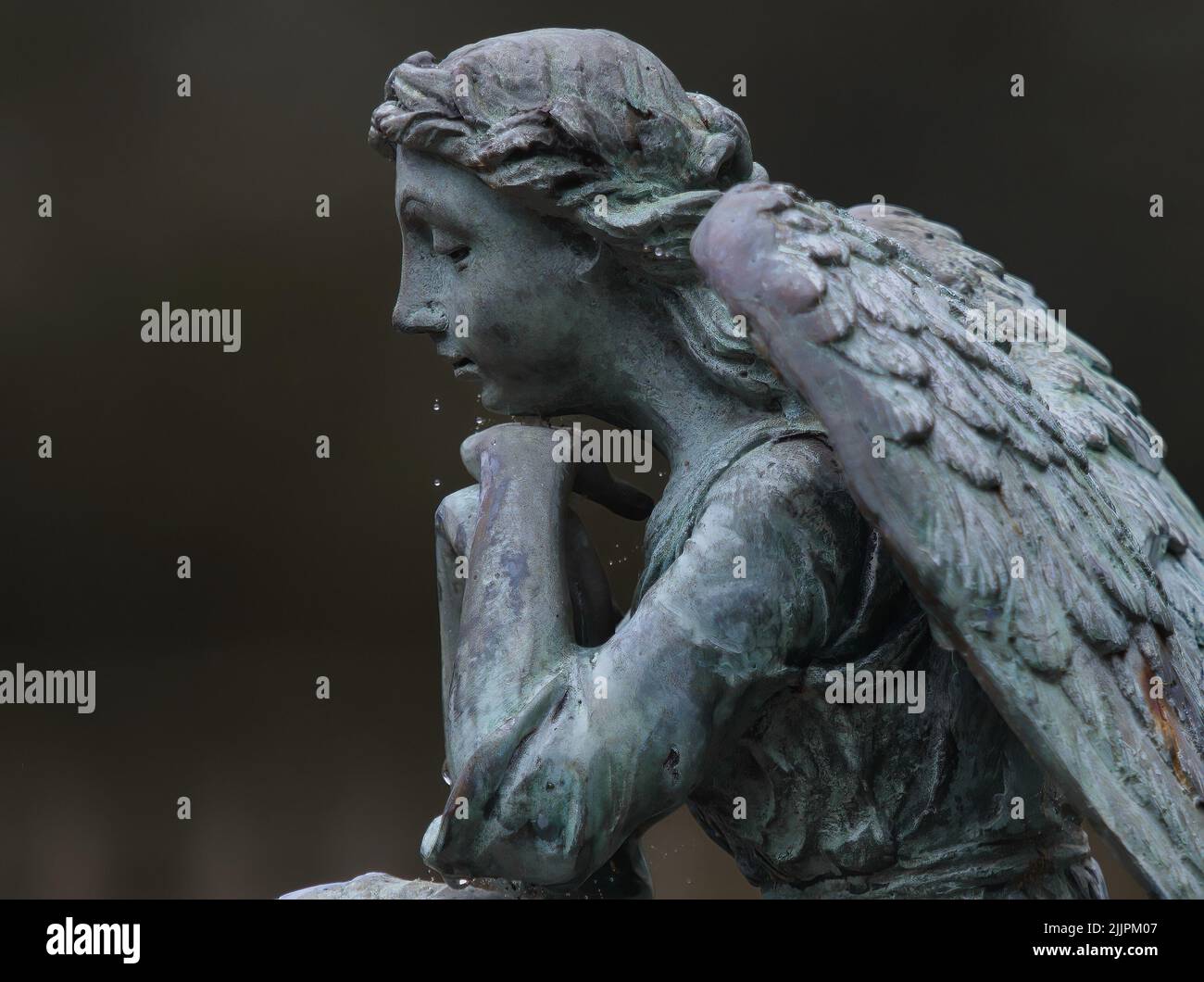 Ein Profil einer weinenden Engelsstatue auf dunklem, verschwommenem Hintergrund. Stockfoto Ein Profil einer weinenden Engelsstatue auf dunklem, verschwommenem Hintergrund. Stockfoto