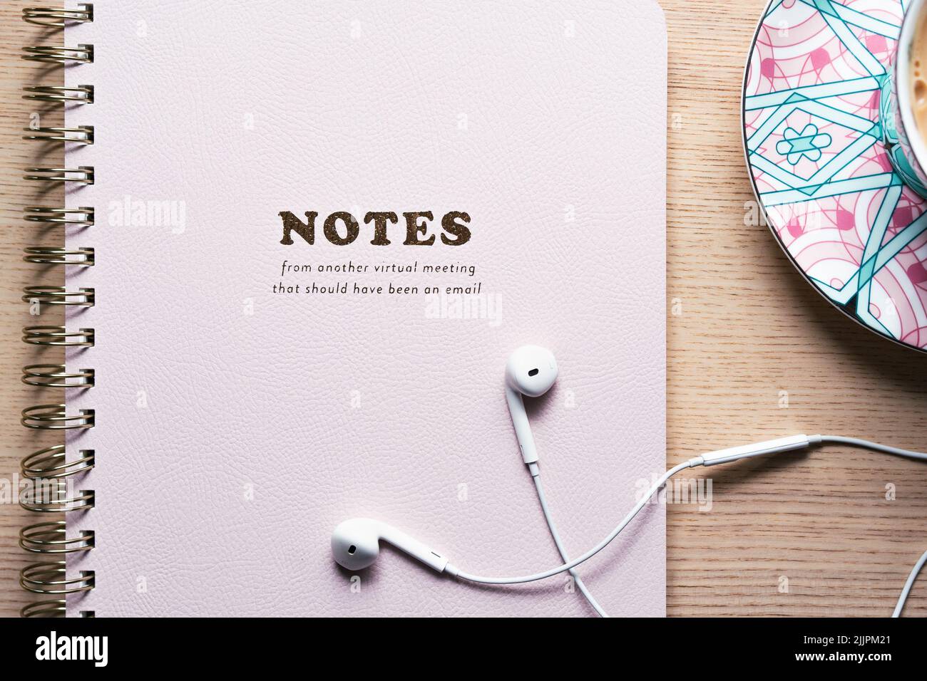 Notebook auf dem Tisch liegend mit weißen Kopfhörern und einer Tasse Tee in einer Teetasse, rosa, Bürobedarf Stockfoto
