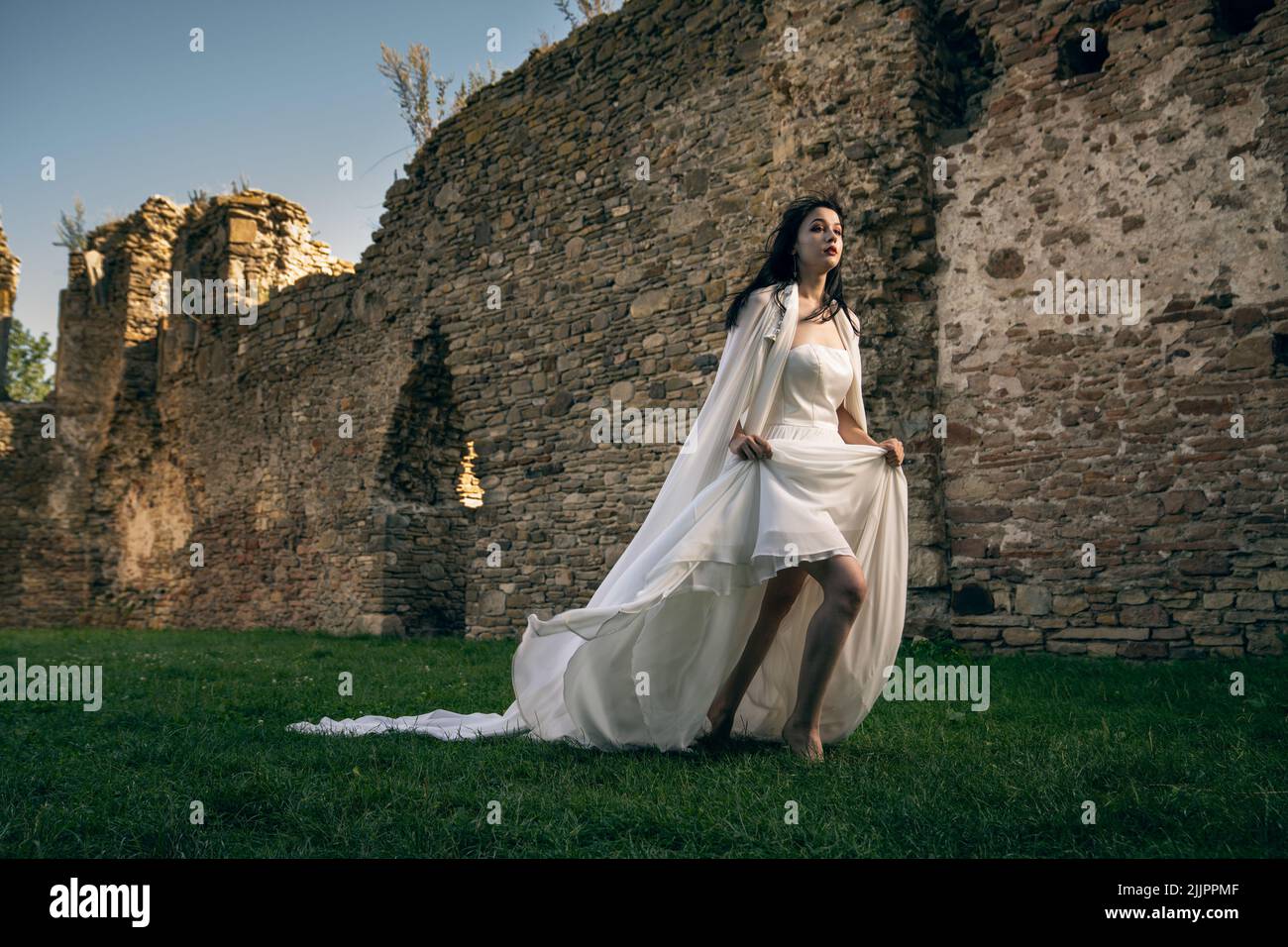 Eine schöne Aufnahme einer kaukasischen Frau in einem eleganten weißen Kleid, das sich in der Nähe einiger uralter Ruinen befindet Stockfoto