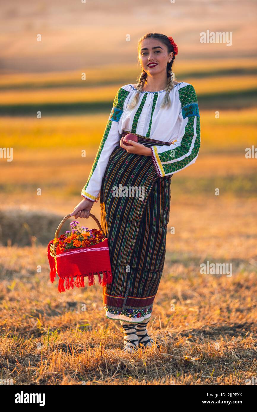 Eine schöne Aussicht auf eine junge Frau mit rumänischer traditioneller Kleidung, die auf dem Feld steht Stockfoto