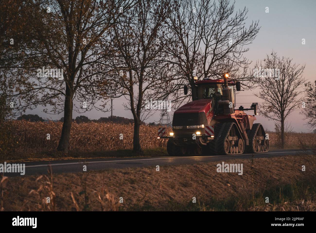 Ein roter Traktor, der am Abend auf einer leeren Straße unterwegs ist Stockfoto