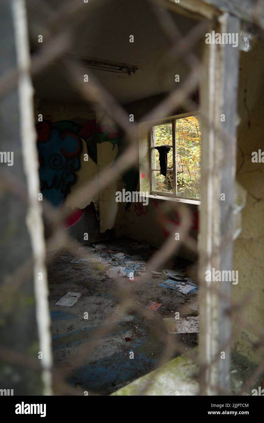 Eine vertikale Aufnahme eines verlassenen Raumes mit Graffiti und schmutzigen Papieren auf dem Boden, hinter einem metallischen Zaun gesehen Stockfoto