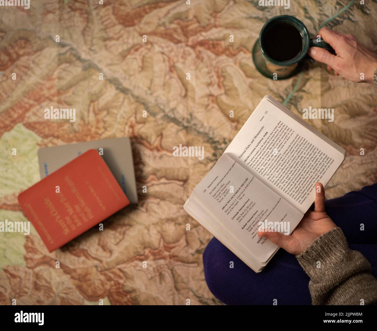 Die Hände einer Person, die einen Reiseführer und eine Tasse Kaffee mit Reiseführern und einer Karte im Hintergrund hält Stockfoto