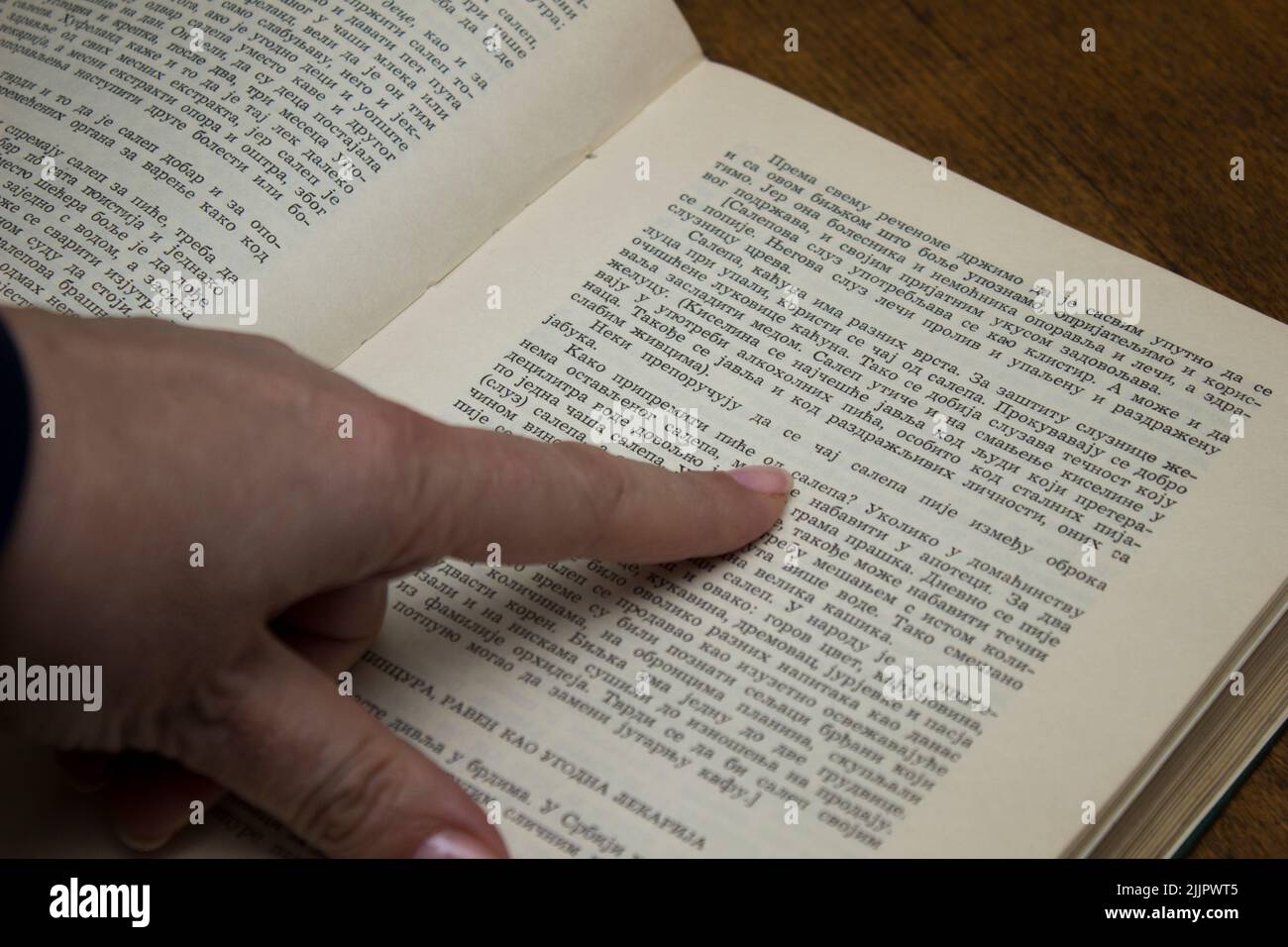 Ein kaukasischer Finger, der das Lesen eines Buches auf Serbisch begleitet Stockfoto