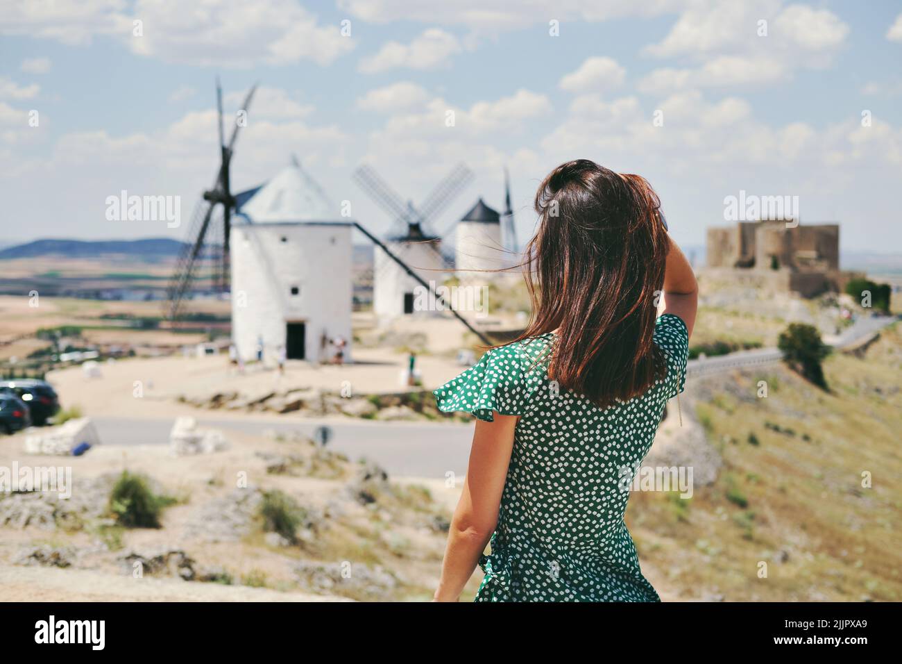 Eine Rückansicht einer jungen Frau, die in der spanischen Stadt Consuegra gegen berühmte alte Windmühlen posiert Stockfoto