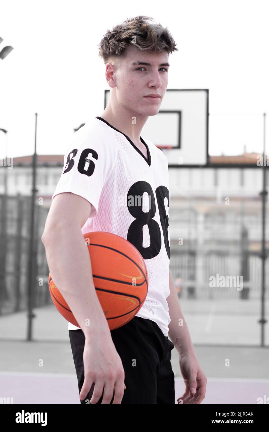Ein Vertikal eines jungen kaukasischen Basketballspielers, der einen Basketball hält, der auf dem Platz steht Stockfoto