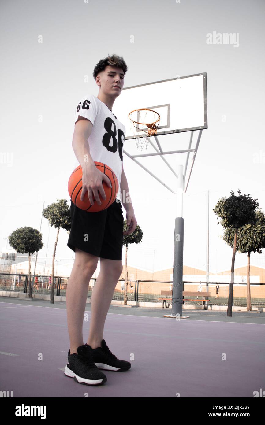 Ein Vertikal eines jungen kaukasischen Basketballspielers, der einen Basketball hält, der auf dem Platz steht Stockfoto