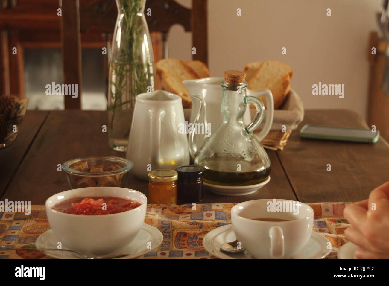 Ein Holztisch mit Tassen, Teekannen, Brot, einem Telefon und anderen Zutaten darauf Stockfoto