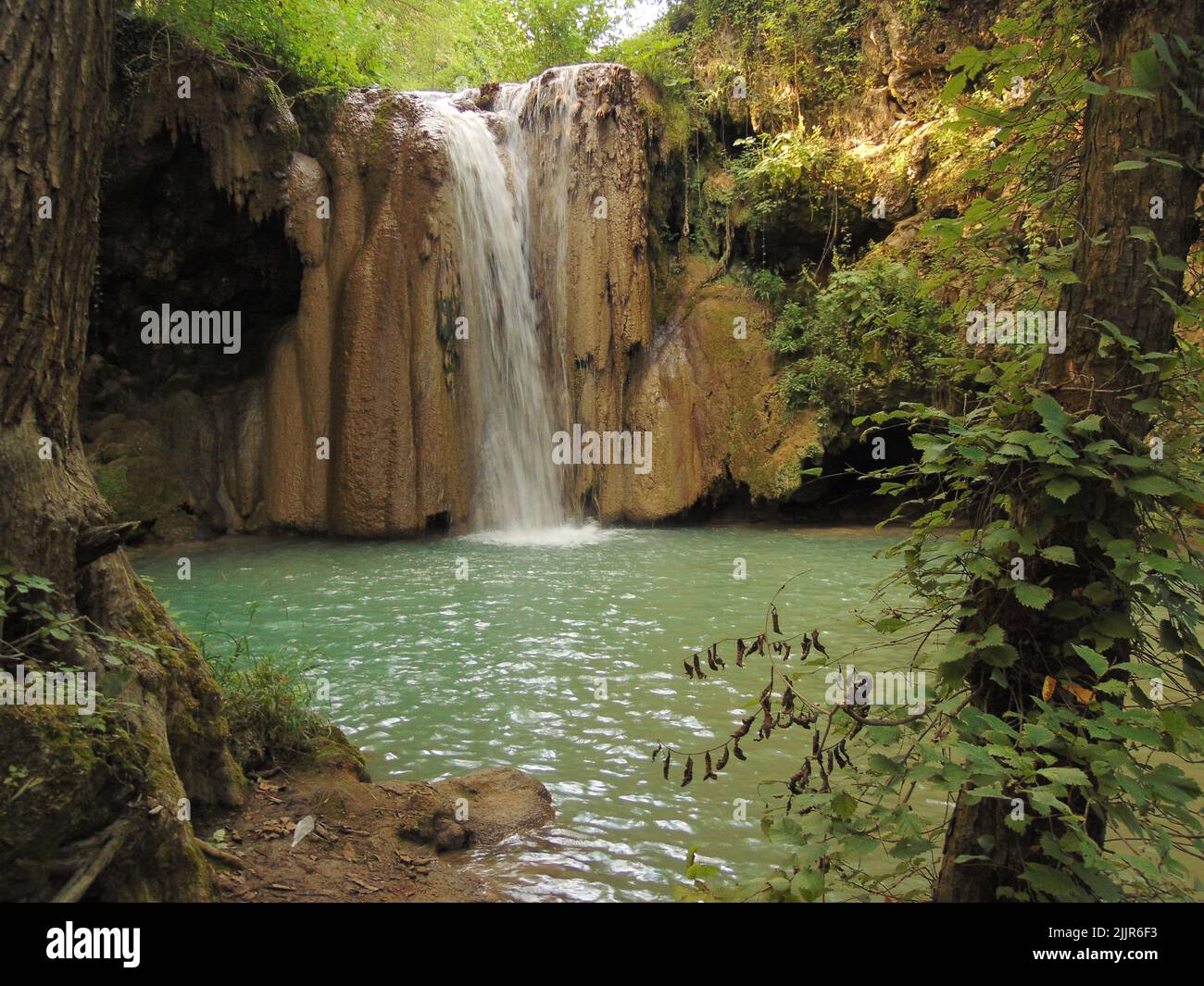 Ein kleiner Bergwasserfall im Wald, der in einen grünen See fließt Stockfoto