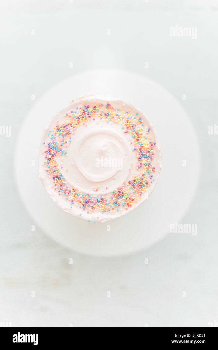 Eine vertikale Draufsicht auf einen hellrosa Kuchen mit Streuseln auf weißem Hintergrund Stockfoto
