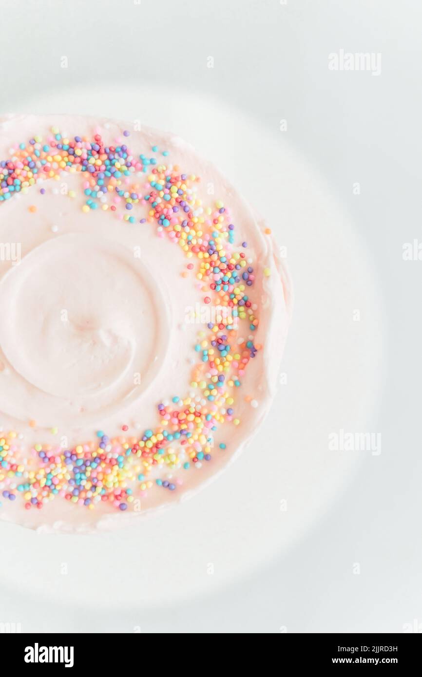 Eine vertikale Draufsicht auf einen hellrosa Kuchen mit Streuseln auf weißem Hintergrund Stockfoto