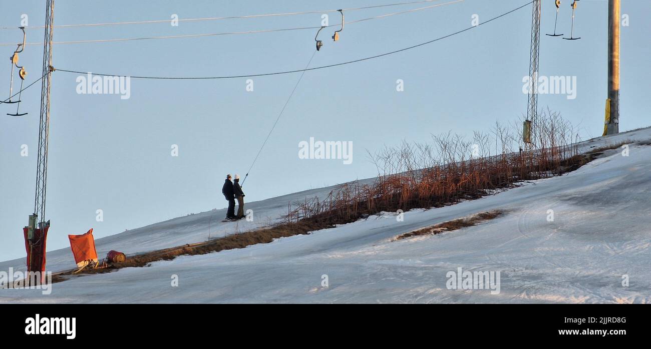 Die beiden Menschen besteigen einen schneebedeckten Berg mit einem Aufzug Stockfoto